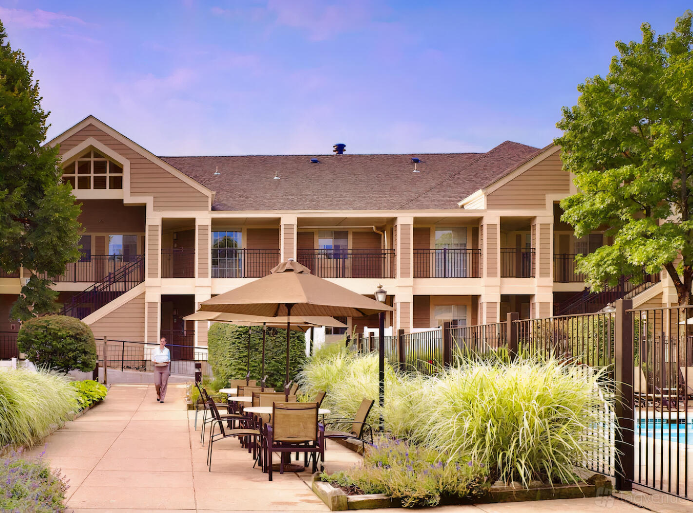 A hotel courtyard with patio tables under umbrellas, lush landscaping, and exterior walkways at Sonesta.