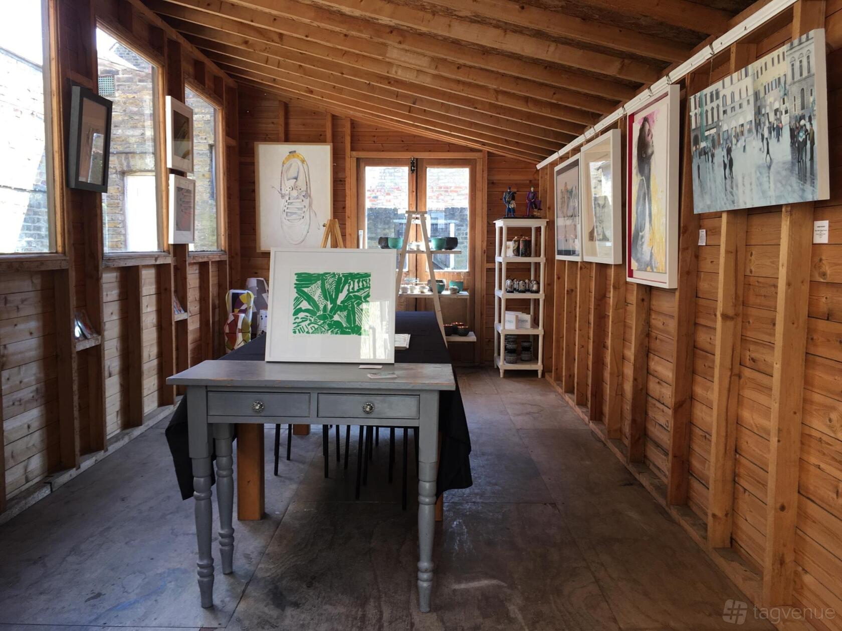 A wooden gallery space with art displayed on natural timber walls and a central table at Ad Lib Gallery, 10 Church Road.