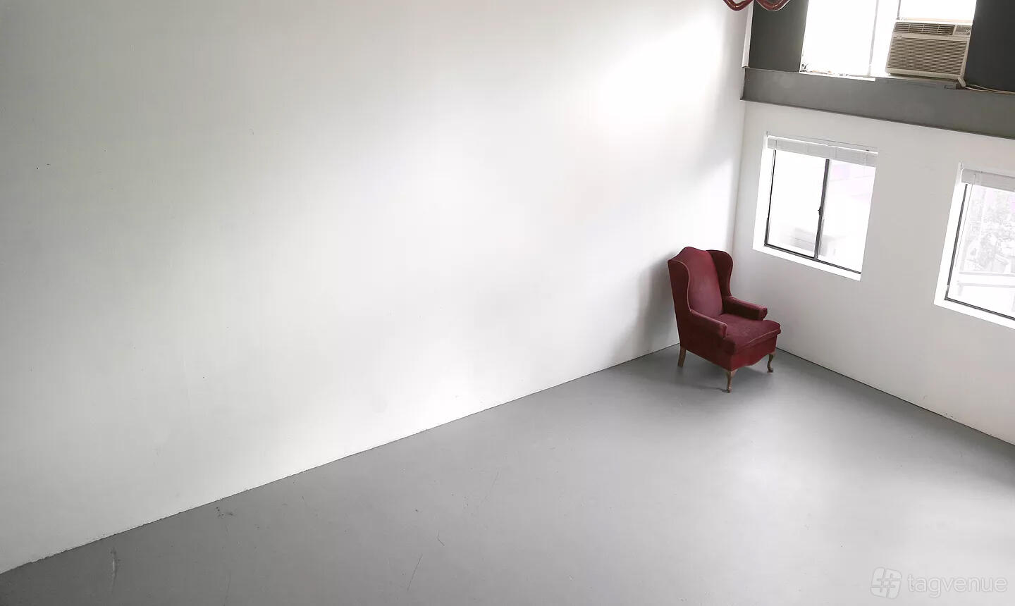 A photo studio with a plain white wall, large windows, and a single red armchair at Studio I at the Brewery Arts Complex.