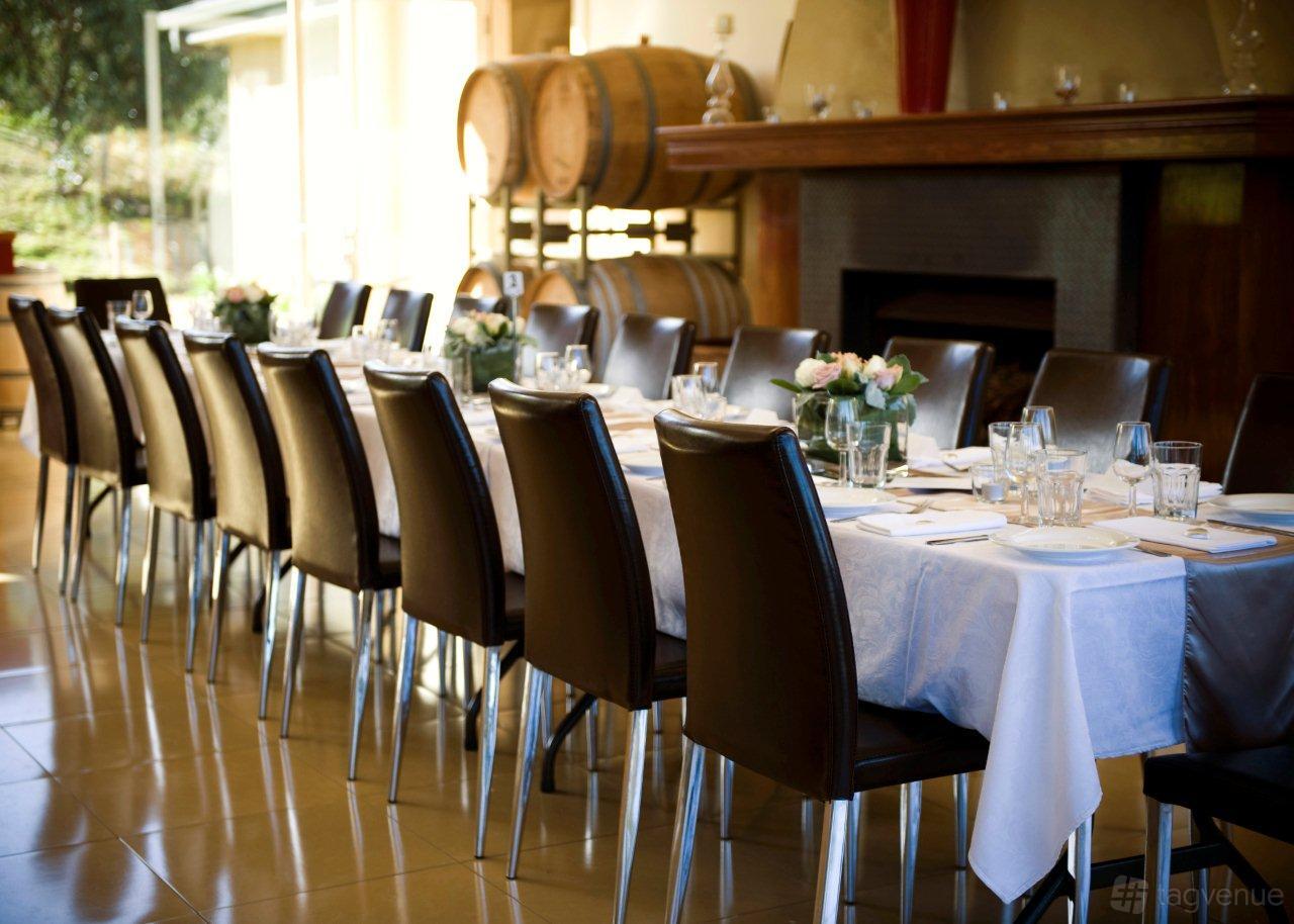 An event space in a winery with a long dining table, dark chairs, and wine barrels at Sutherland Estate.