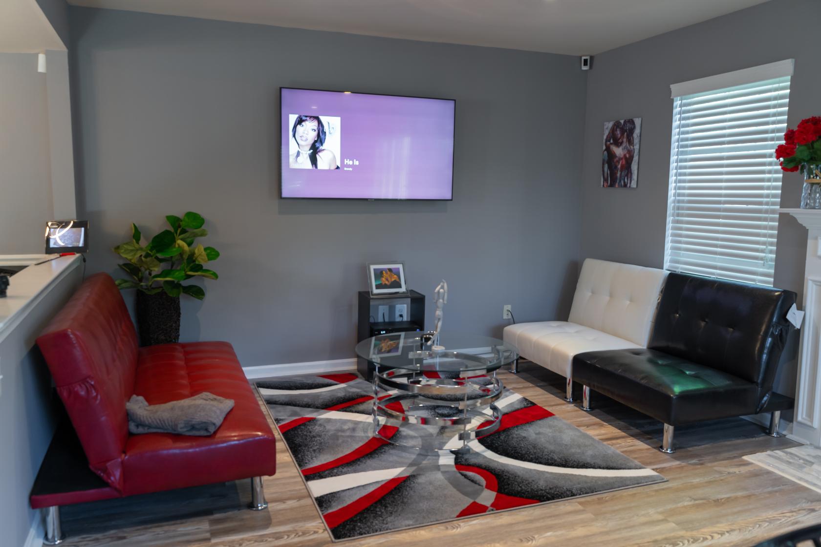An apartment living room with leather sofas, a patterned rug, and a wall-mounted TV at KNKY House.