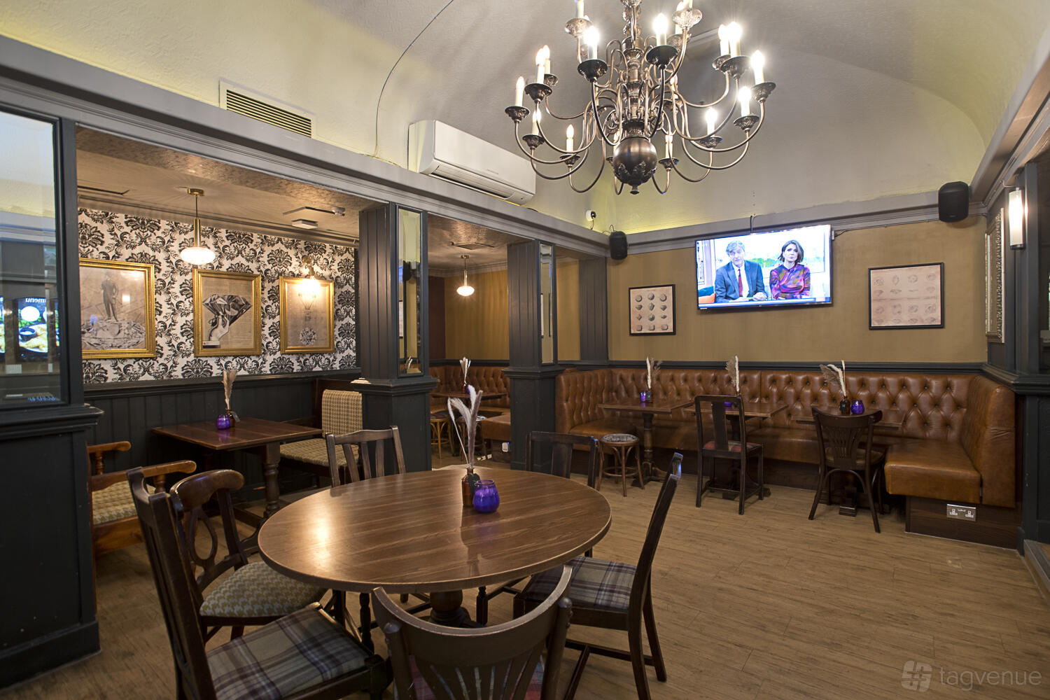 A pub with tufted leather booths, wooden tables, a chandelier, and patterned wallpaper at The Argyle.