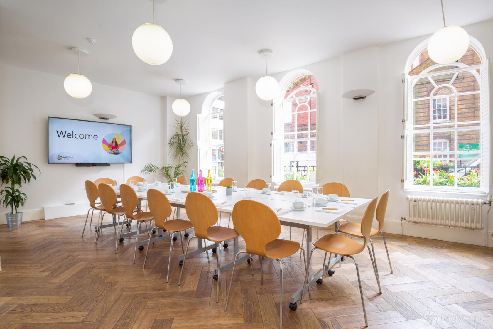 A function room with large arched windows, parquet flooring, and a boardroom table setup at Fitzrovia Community Centre.