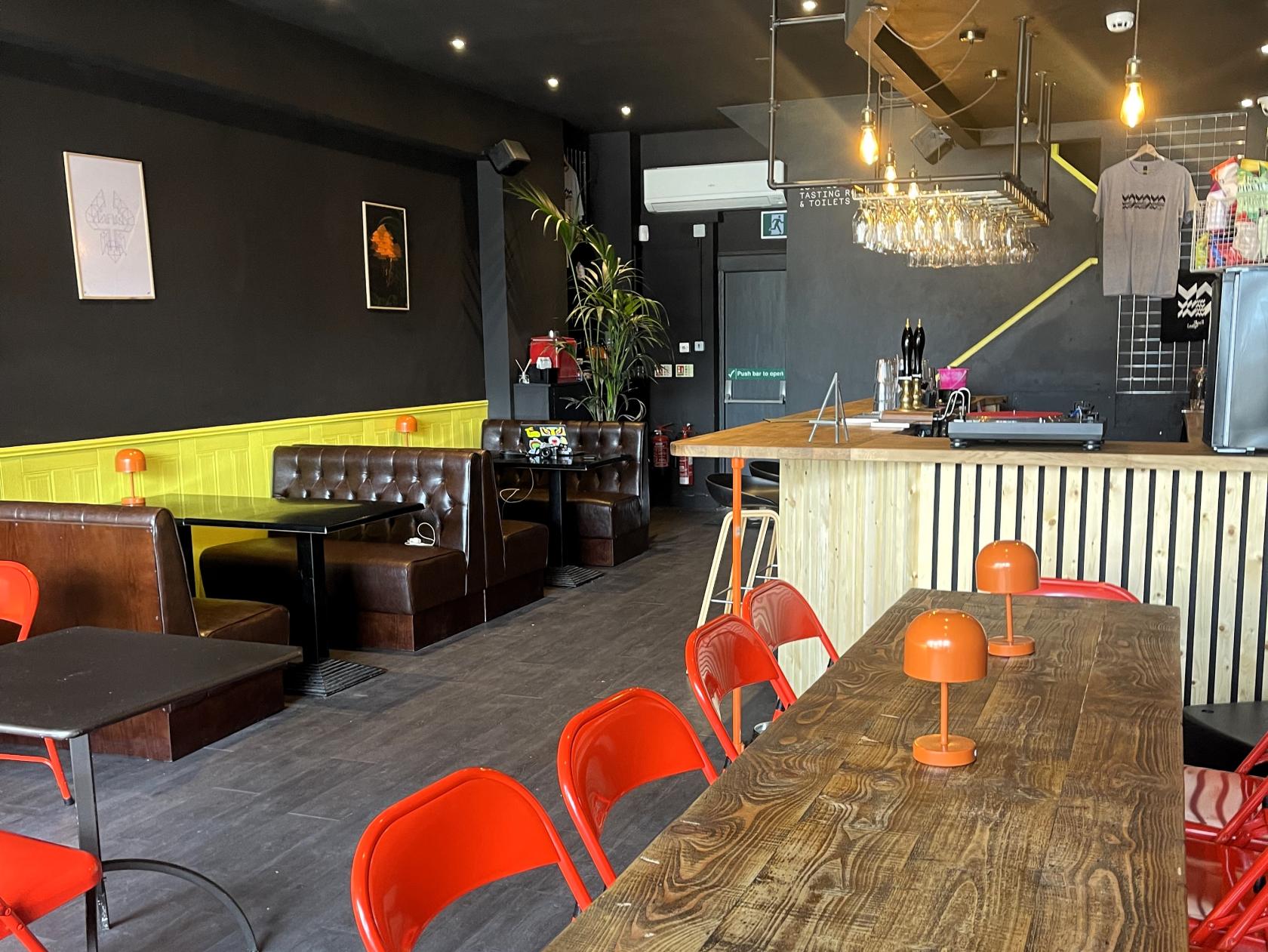 A dining room with wooden tables, red chairs, orange table lamps, and booth seating at Black Lodge West Kirby.