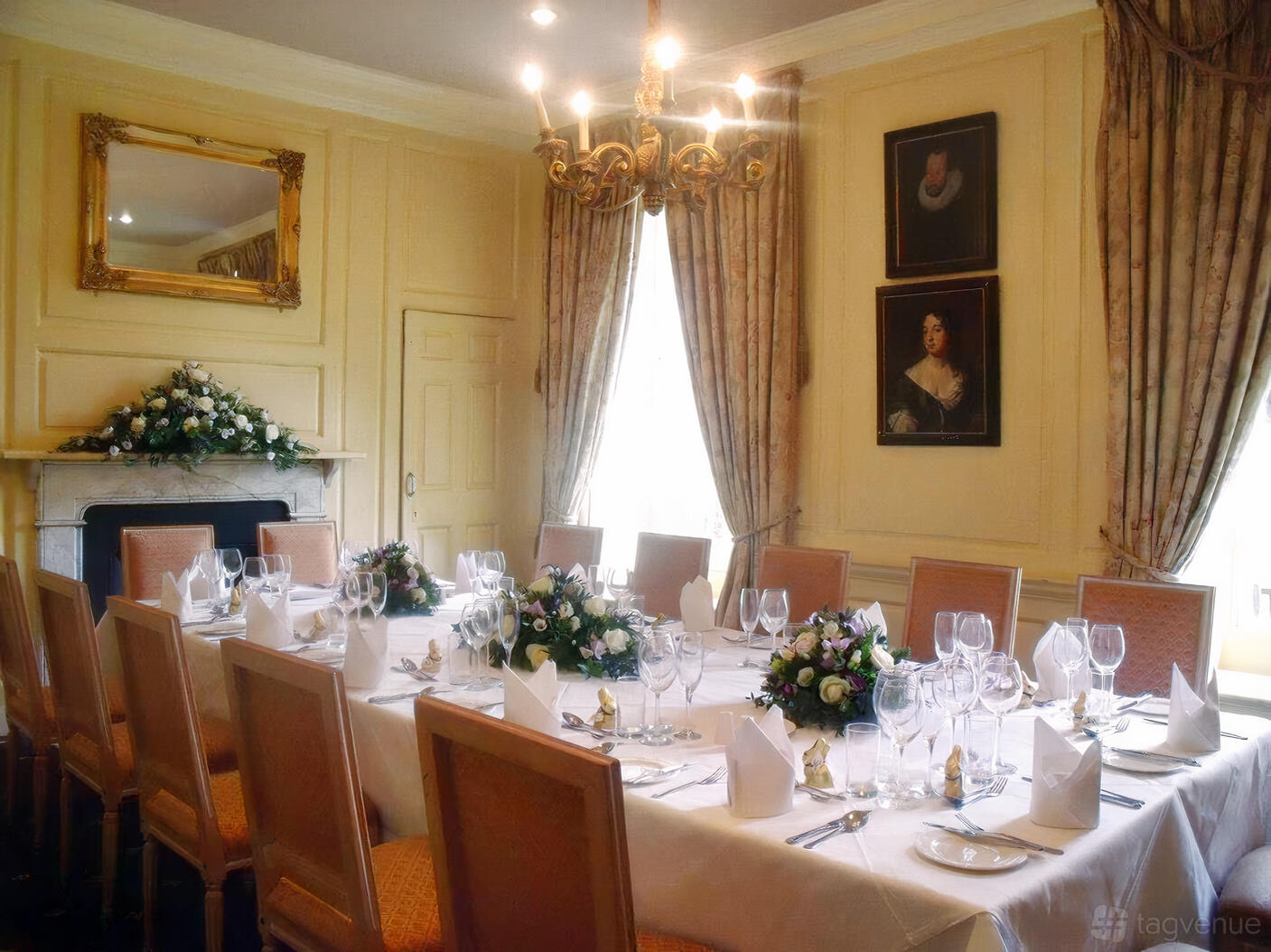 A dining room with a long table set for a formal meal, floral centerpieces, and a chandelier at Hintlesham Hall Hotel.