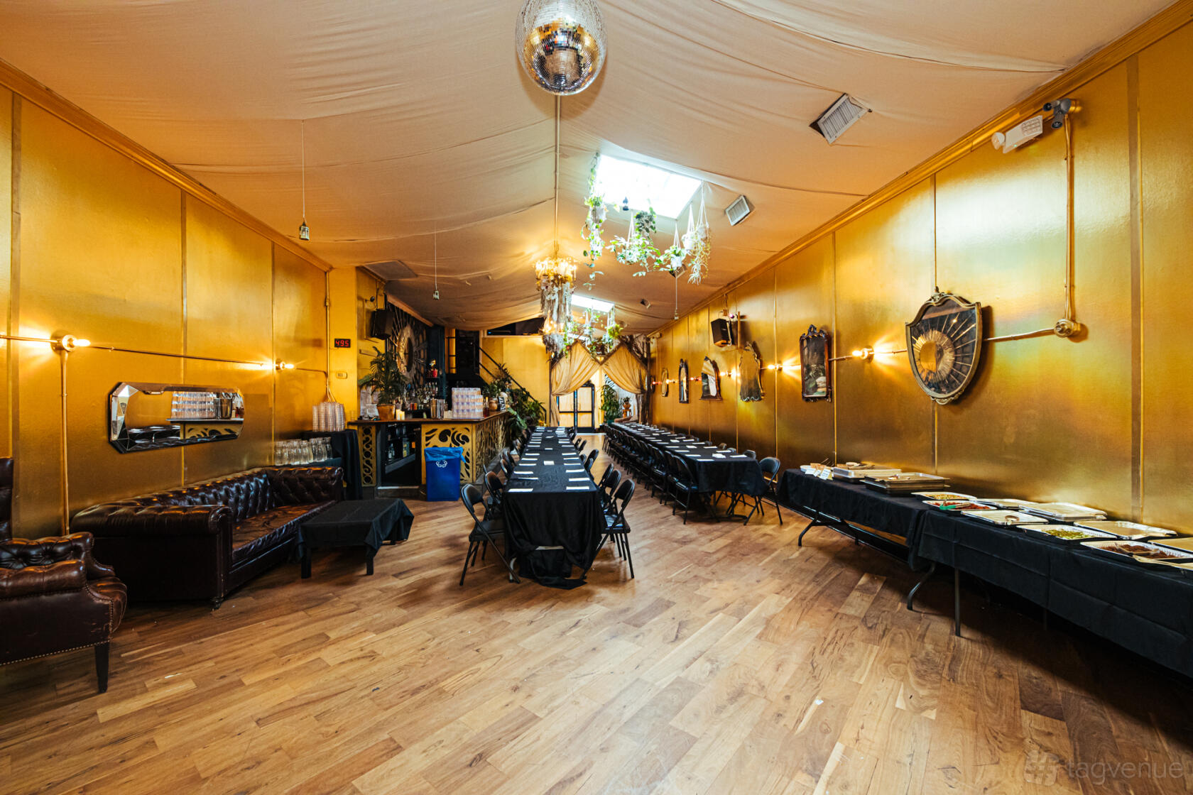 An event space with gold walls, a mirrored disco ball, chandeliers, and banquet tables at House of Yes.