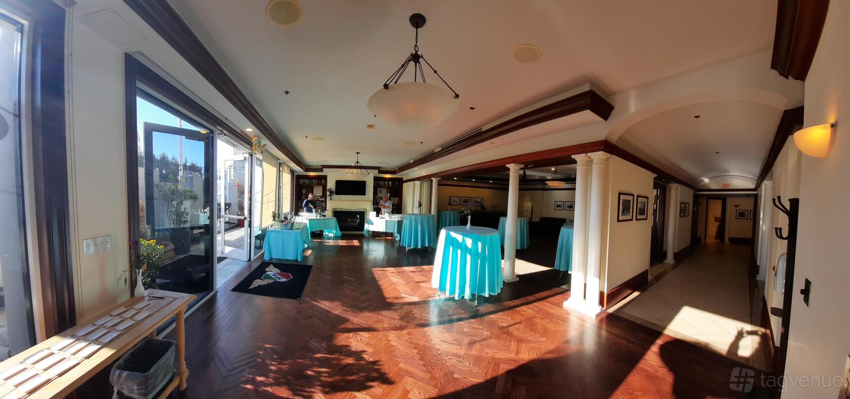 An event venue with large windows, hardwood floors, and cocktail tables with turquoise linens at San Francisco Italian Athletic Club.