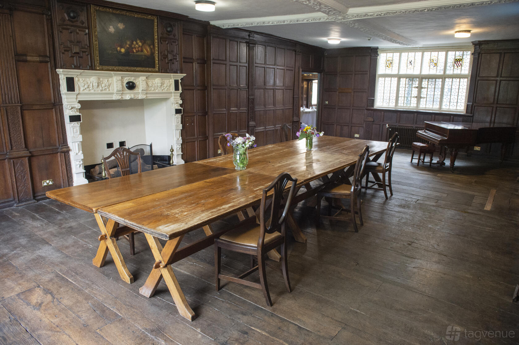 A wood-paneled lounge with a long wooden table, fireplace, and leaded glass window at Rothamsted Manor.