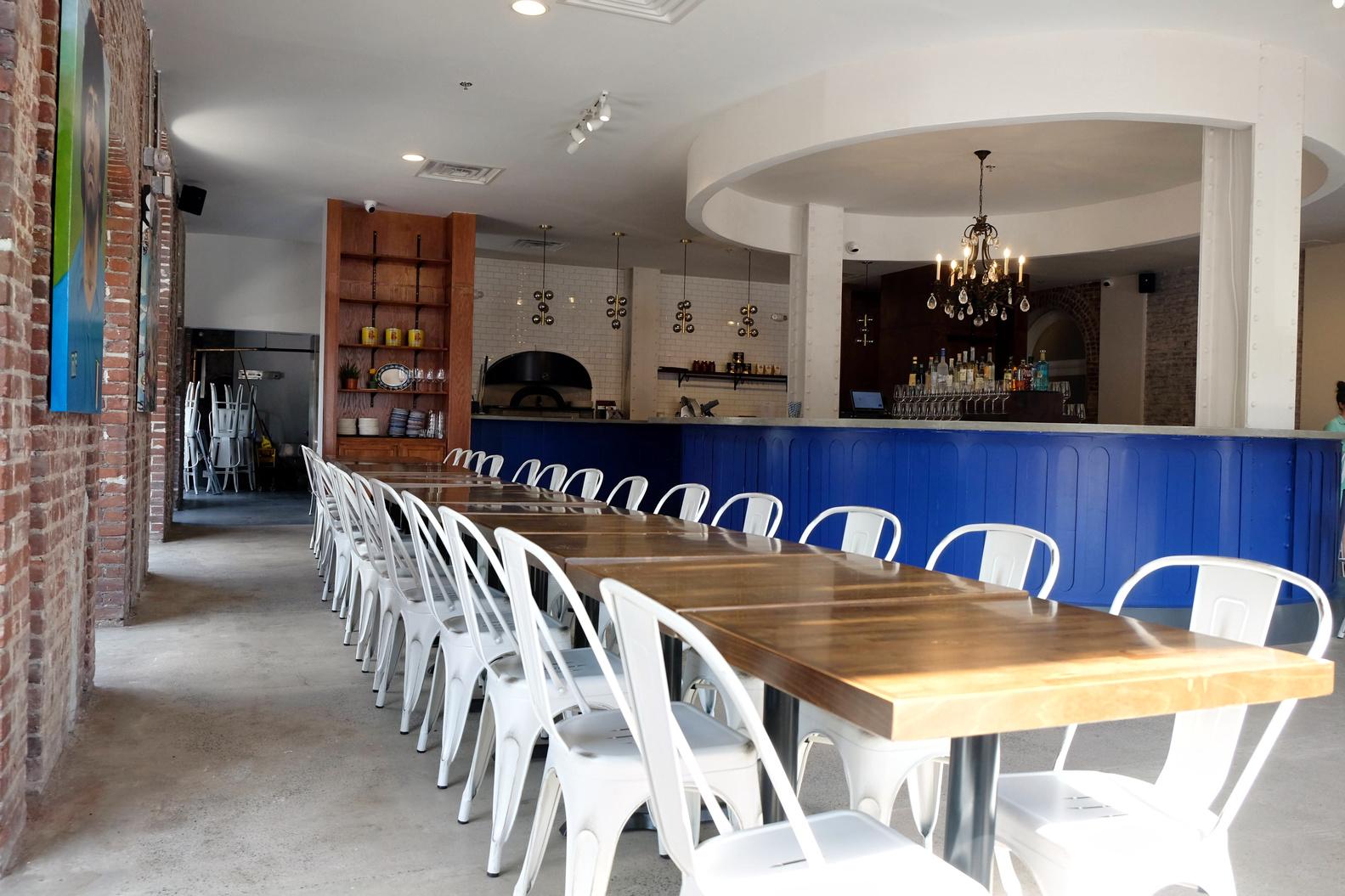 A function room with long wooden tables, white metal chairs, and a blue bar at Cicala at The Divine Lorraine.