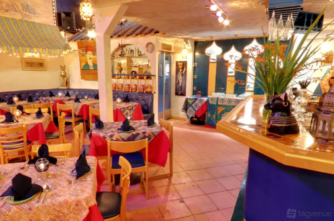 A restaurant with colorful Egyptian decor, patterned tablecloths, and blue cushioned seating at Al-Masri Egyptian Restaurant.