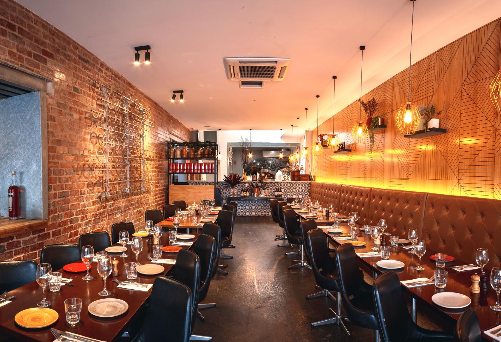 An event space with exposed brick walls, tufted leather banquette seating, and pendant lighting at Rococo.