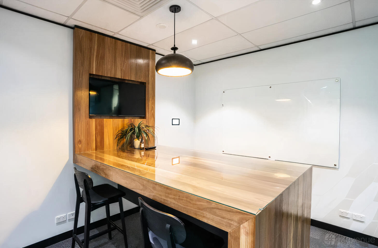 A meeting room with a large wooden table, wall-mounted screen, whiteboard, and pendant lighting at Waterman at Narre Warren.