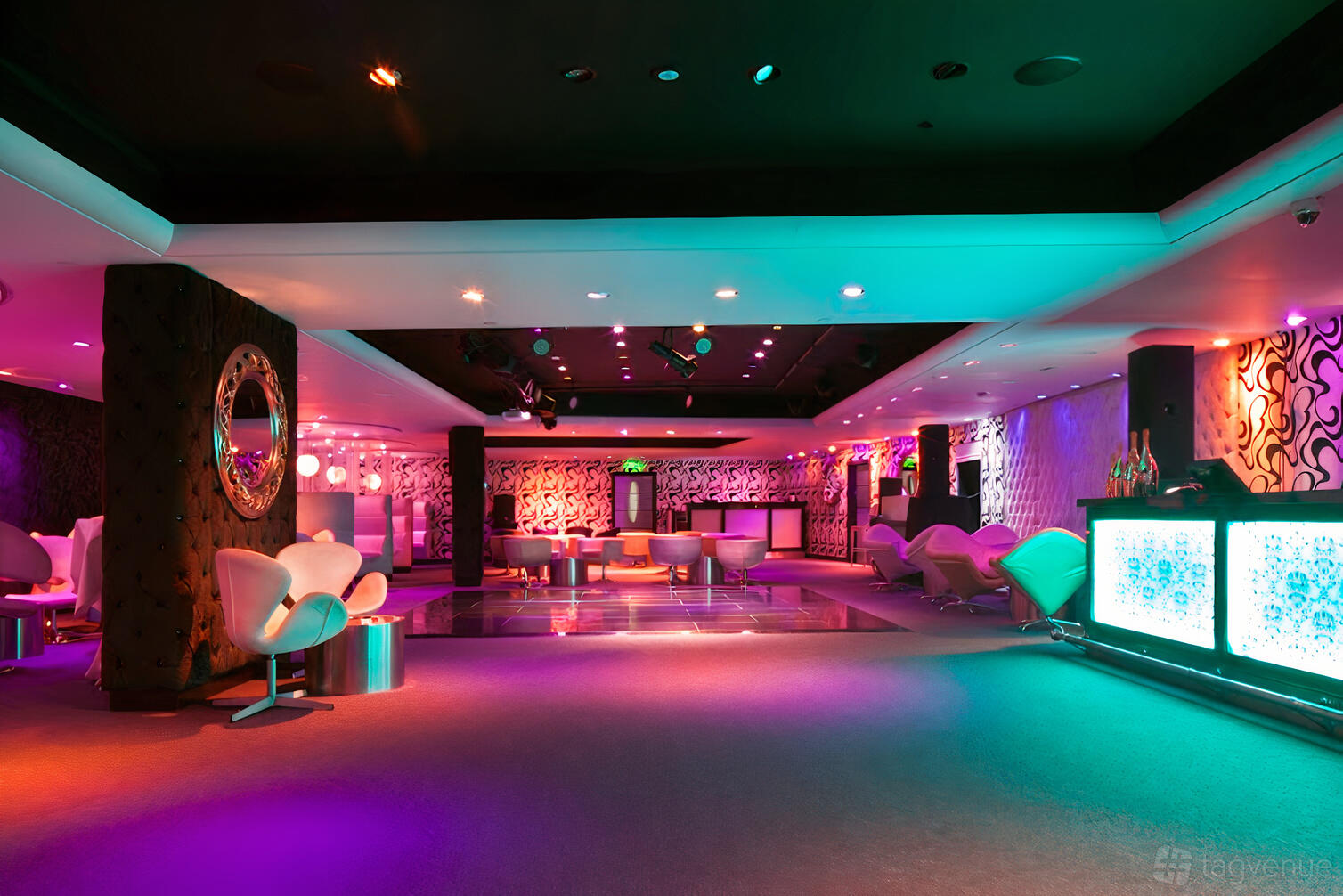 An event space with colorful ambient lighting, lounge seating, and illuminated bar at Leonardo Royal London St Paul's.