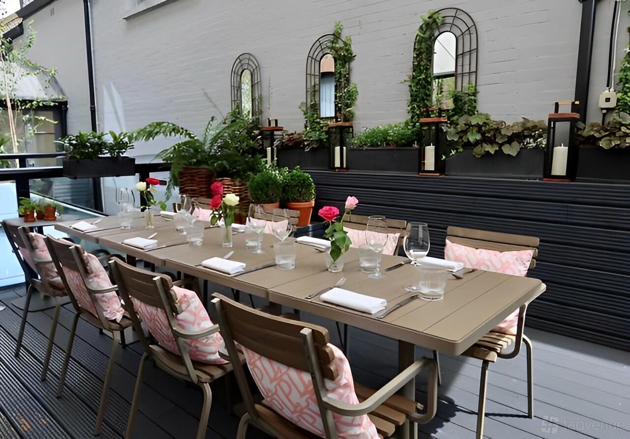 A terrace with a long dining table, cushioned chairs, potted plants, and wall mirrors at 11 Cadogan Gardens.