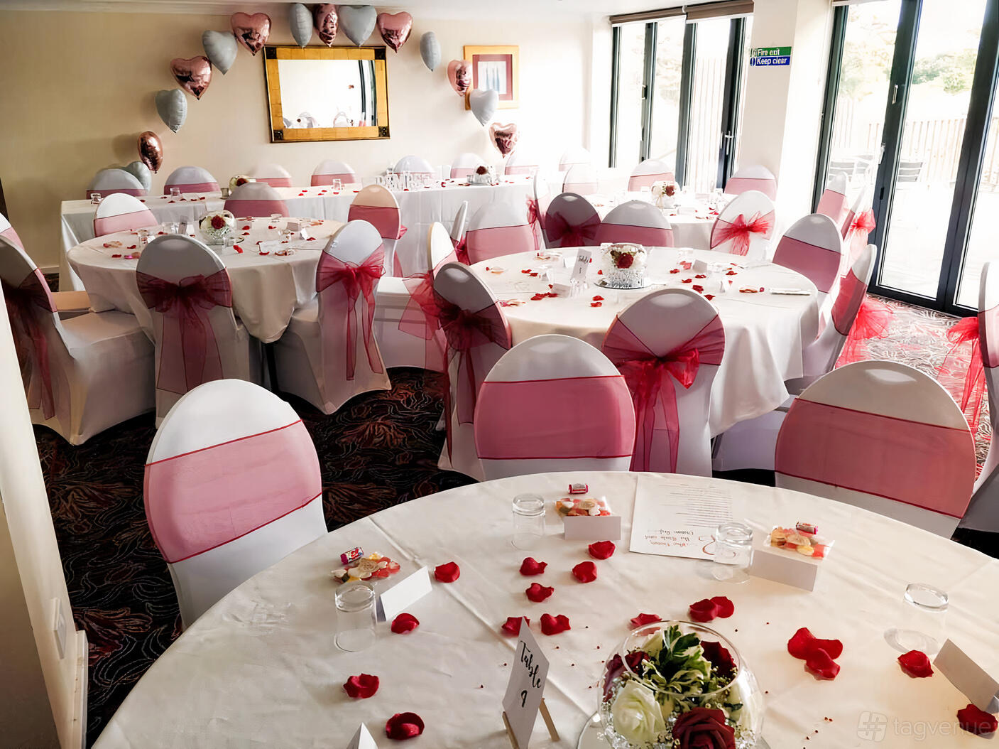 An event space with round tables, white linens, and pink chair sashes set for a celebration at The Bridge House.