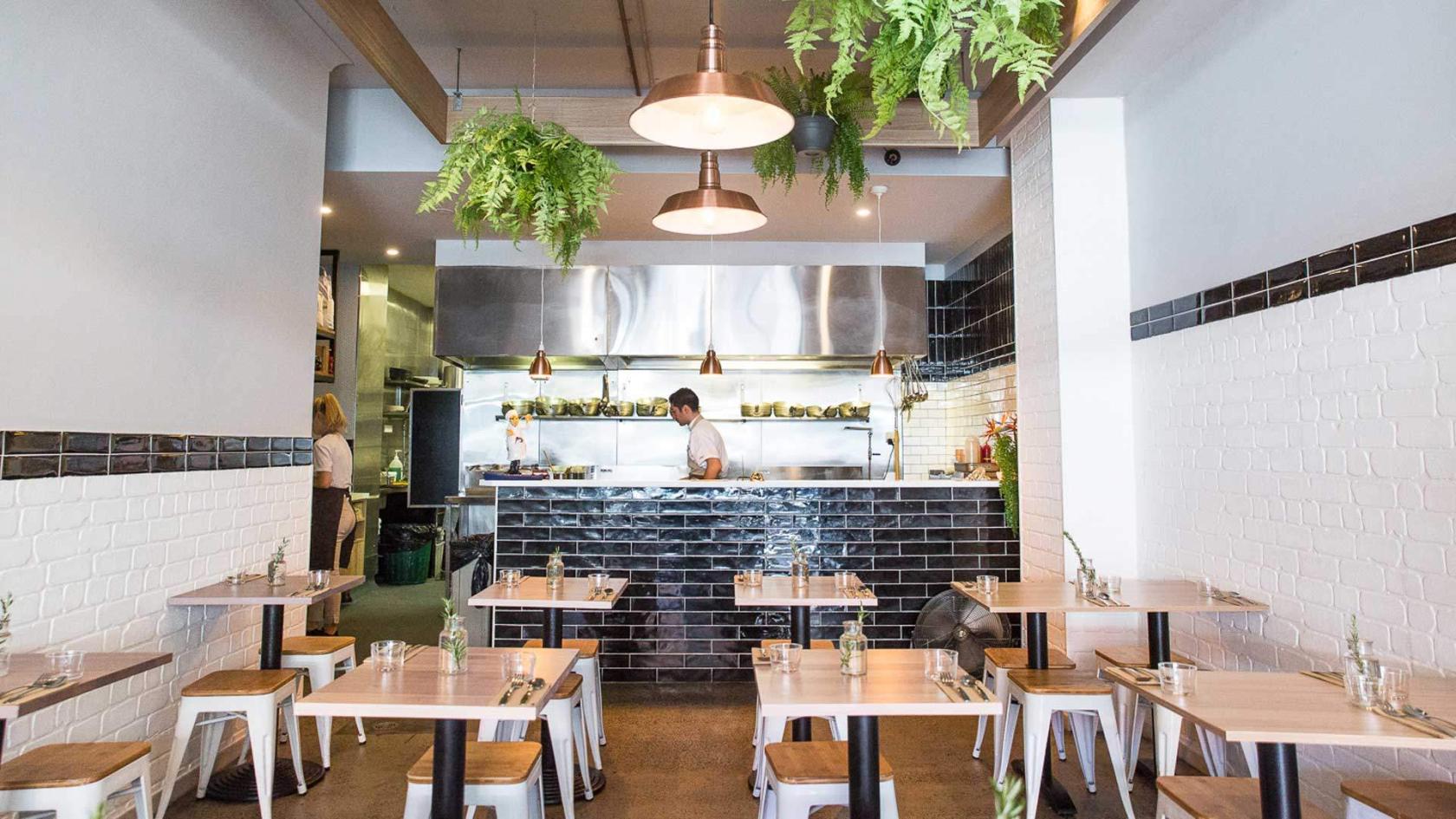 A restaurant with an open kitchen, black tiled counter, hanging plants, and wooden tables at La Favola.