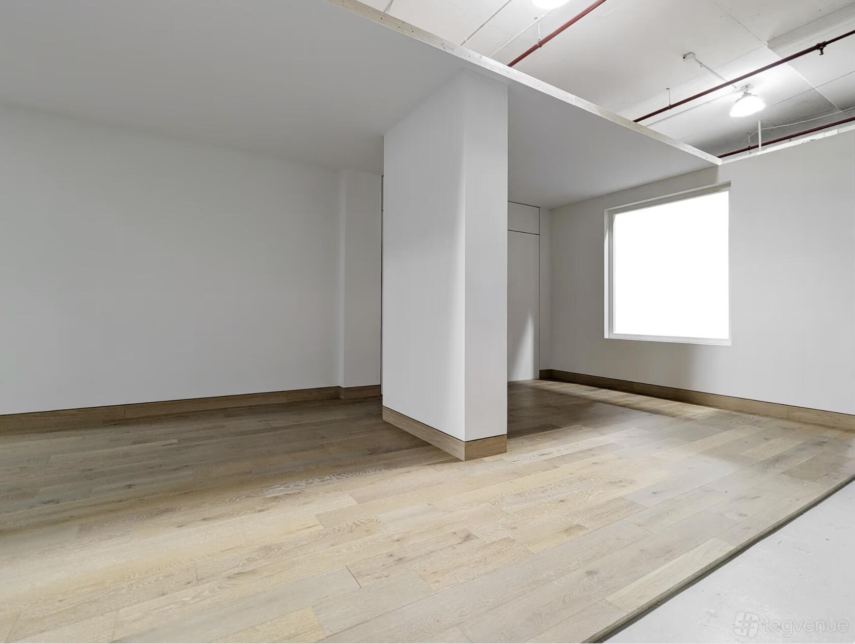 A photo studio with light wood floors, plain white walls, and a large window at Mayo Studios.
