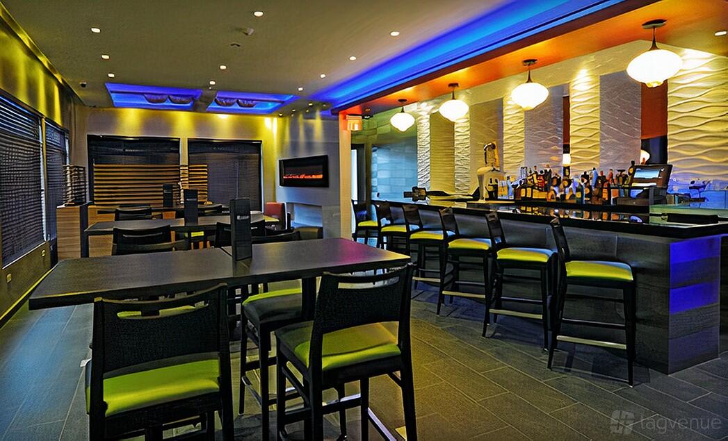 An event space in a restaurant with a backlit bar, textured white walls, and high-top tables at MK Valencia.