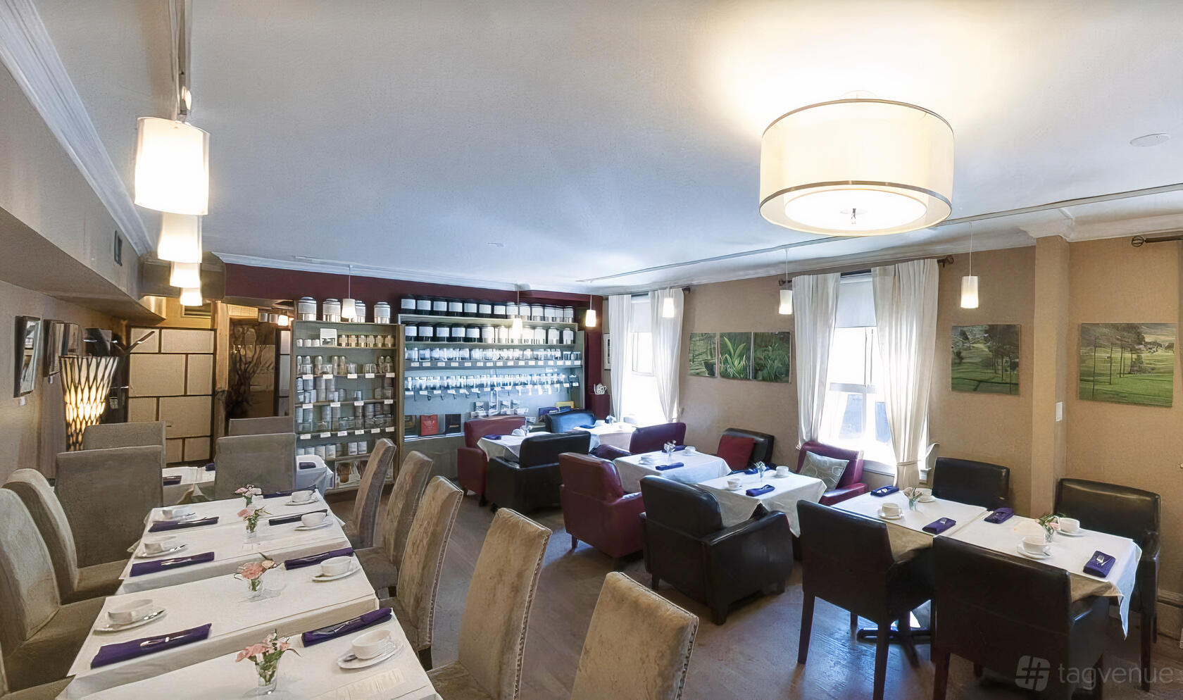 A restaurant lounge with white-clothed tables, plush armchairs, tea canisters on shelves, and natural lighting at t-buds.