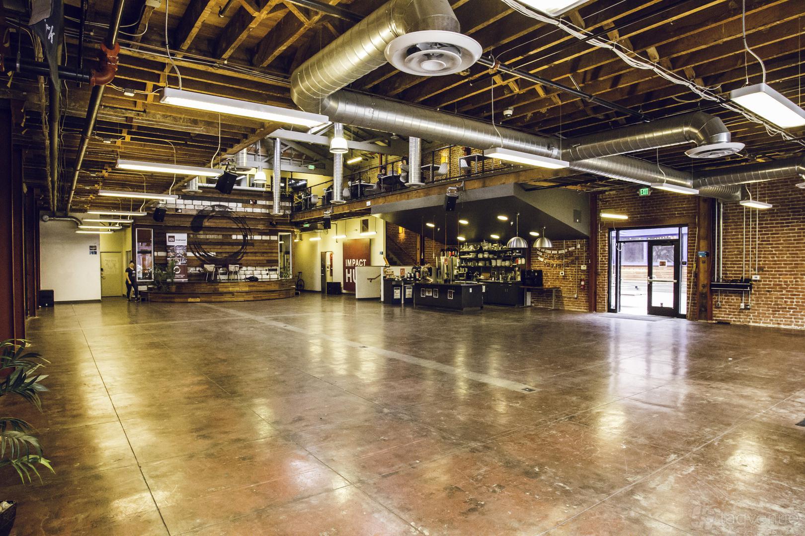 An event hall with exposed brick walls, polished concrete floors, and an open ceiling with visible ductwork at Oakstop 2323 Broadway.