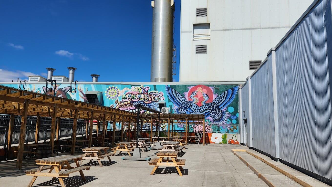 An outdoor brewery with picnic tables, a wood pergola, and a vibrant mural at Collective Ash Brewing.