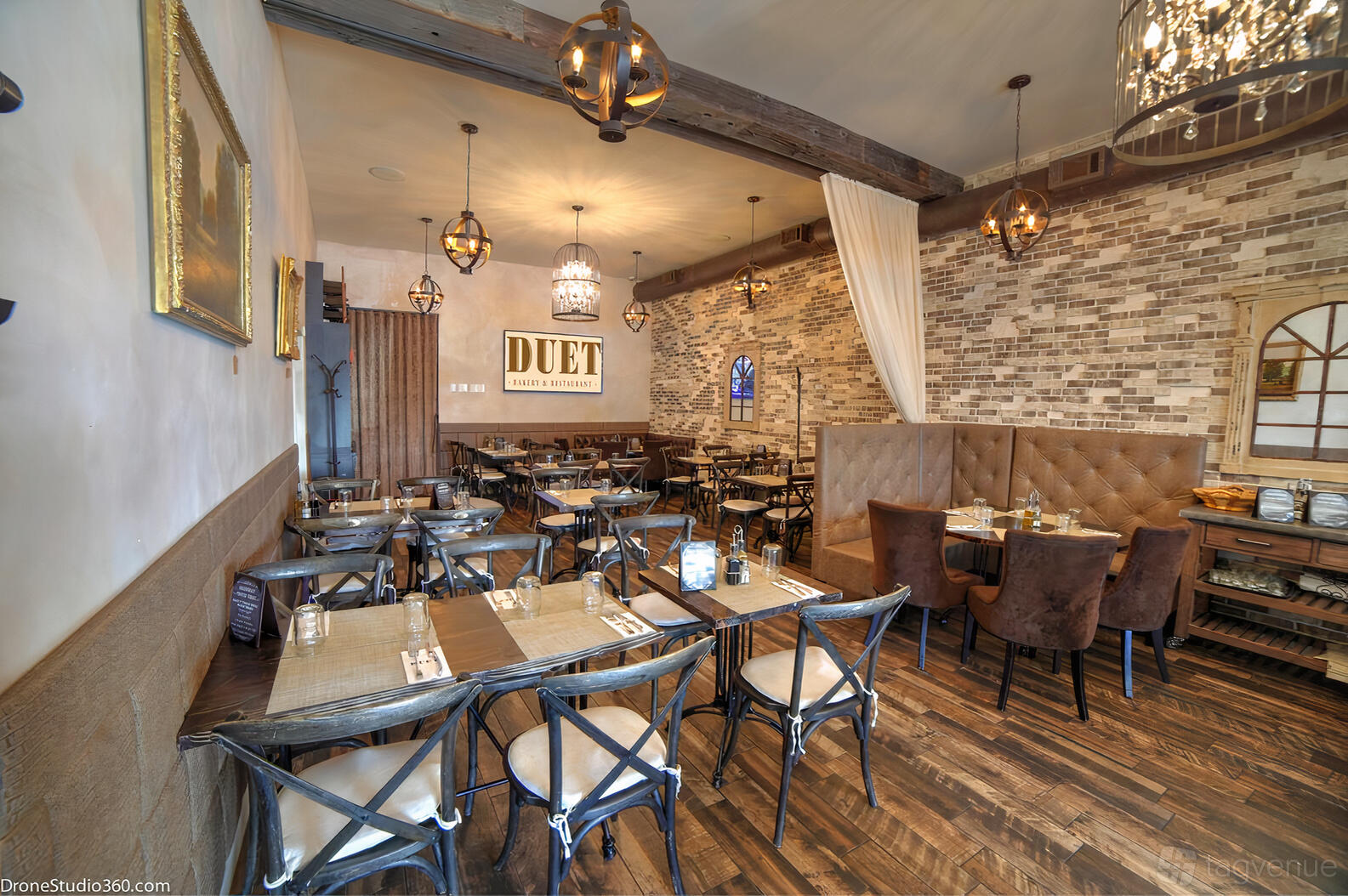 A restaurant with exposed brick walls, wooden floors, pendant lighting, and brown upholstered booths at Duet Bakery and Restaurant.