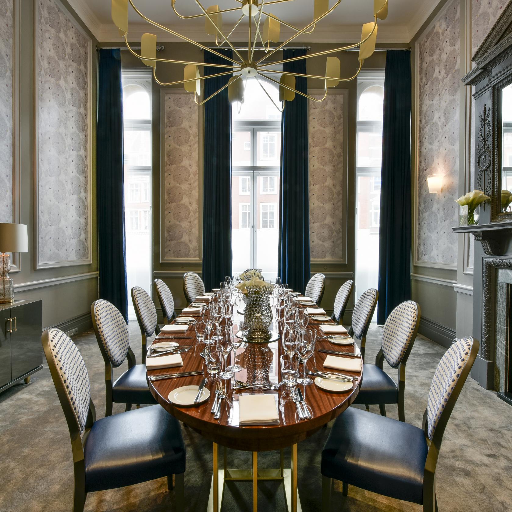 A function room with a polished oval table, patterned chairs, and tall windows with blue curtains at Andaz London Hotel.