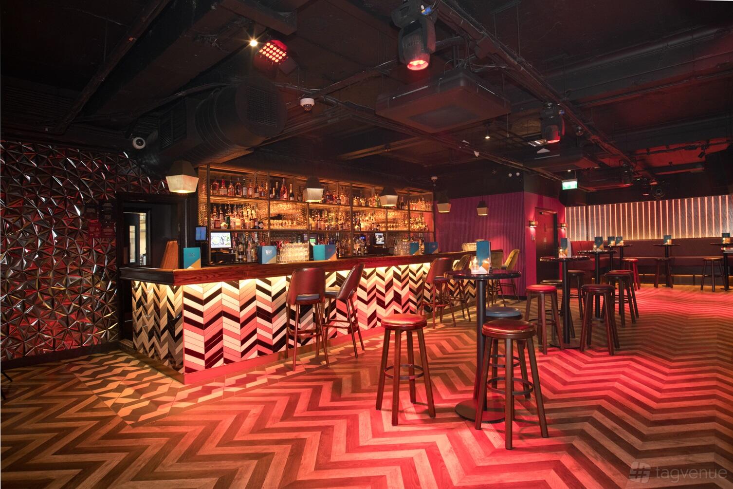 An event space with chevron wood flooring, geometric wall patterns, and a long cocktail bar at Be at One Regent Street.