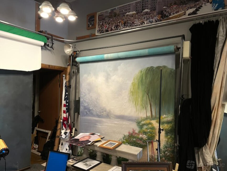 A photo studio with a painted backdrop of a lakeside scene and professional lighting equipment at Kee Studio.