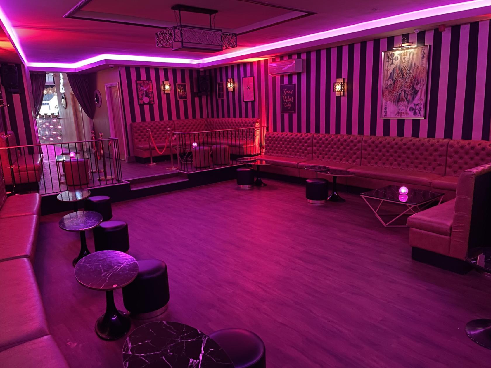 A bar with tufted leather banquettes, striped walls, small round tables, and purple ambient lighting at Parlay E18.