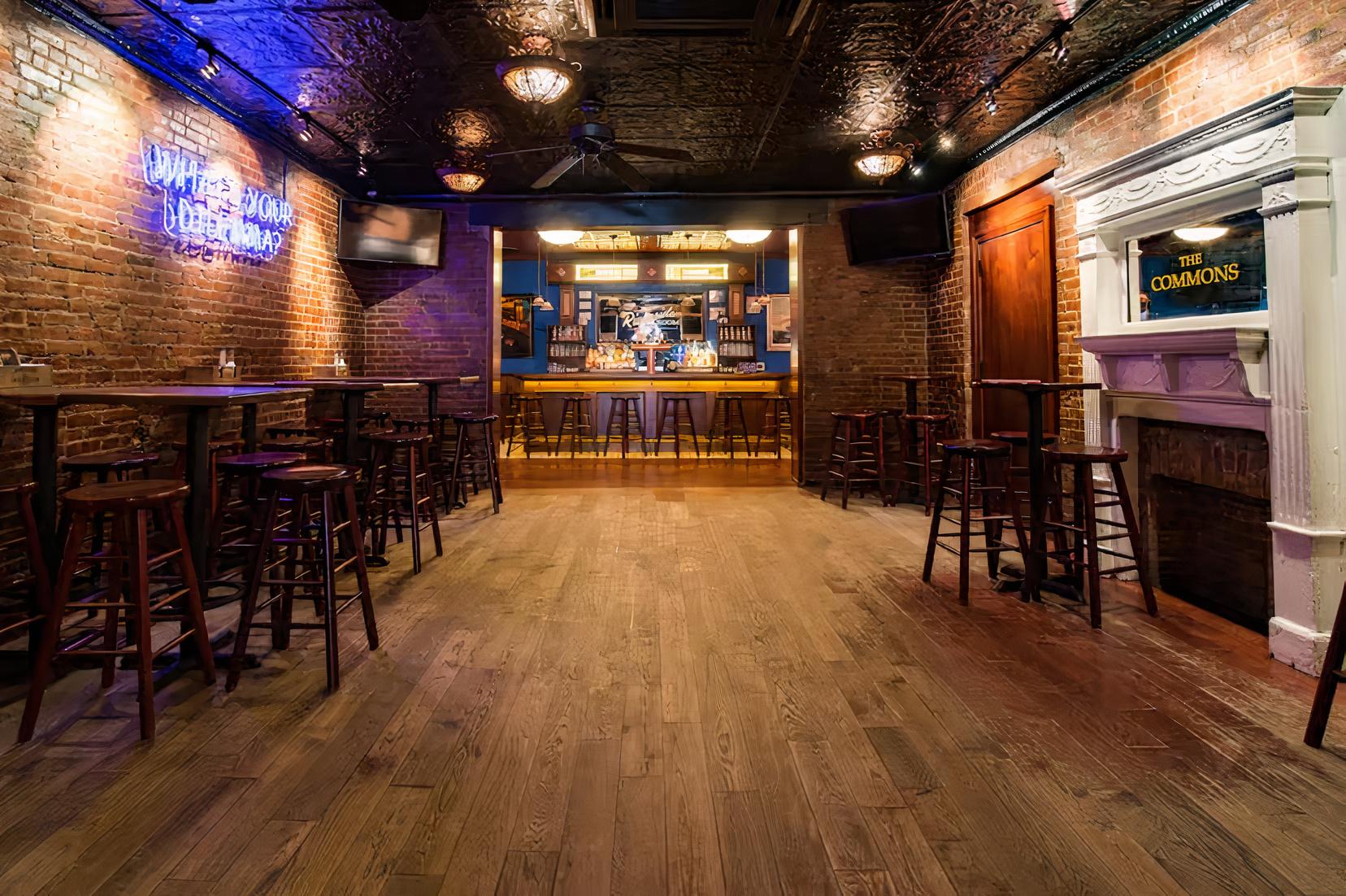 A bar with exposed brick walls, wooden floors, high tables with stools, and a neon sign at Jake's Dilemma.