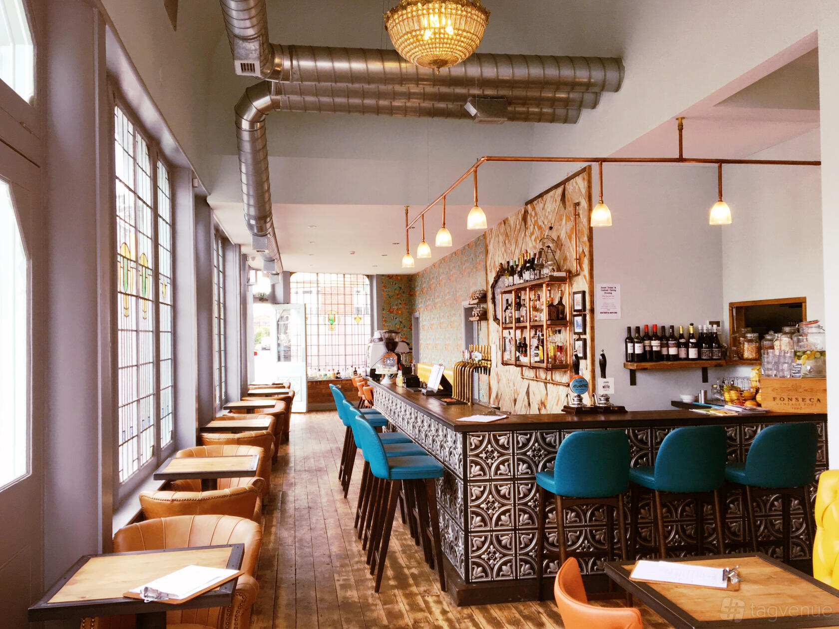 A pub with patterned tile bar, teal barstools, pendant lighting, and window seating at Temper and Brown.