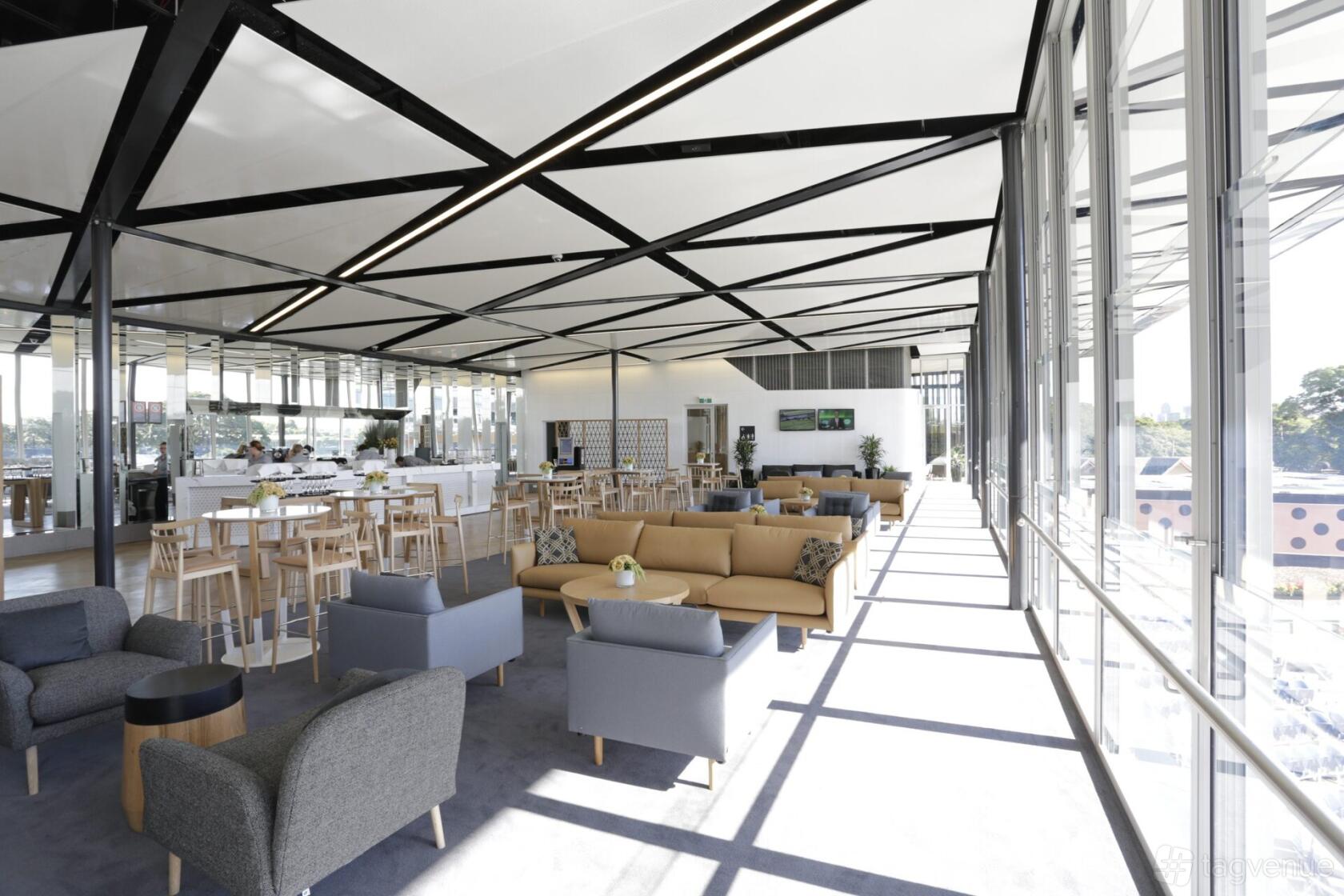 An event venue with floor-to-ceiling windows, beige sofas, and light wood high tables at Australian Turf Club @ Royal Randwick.