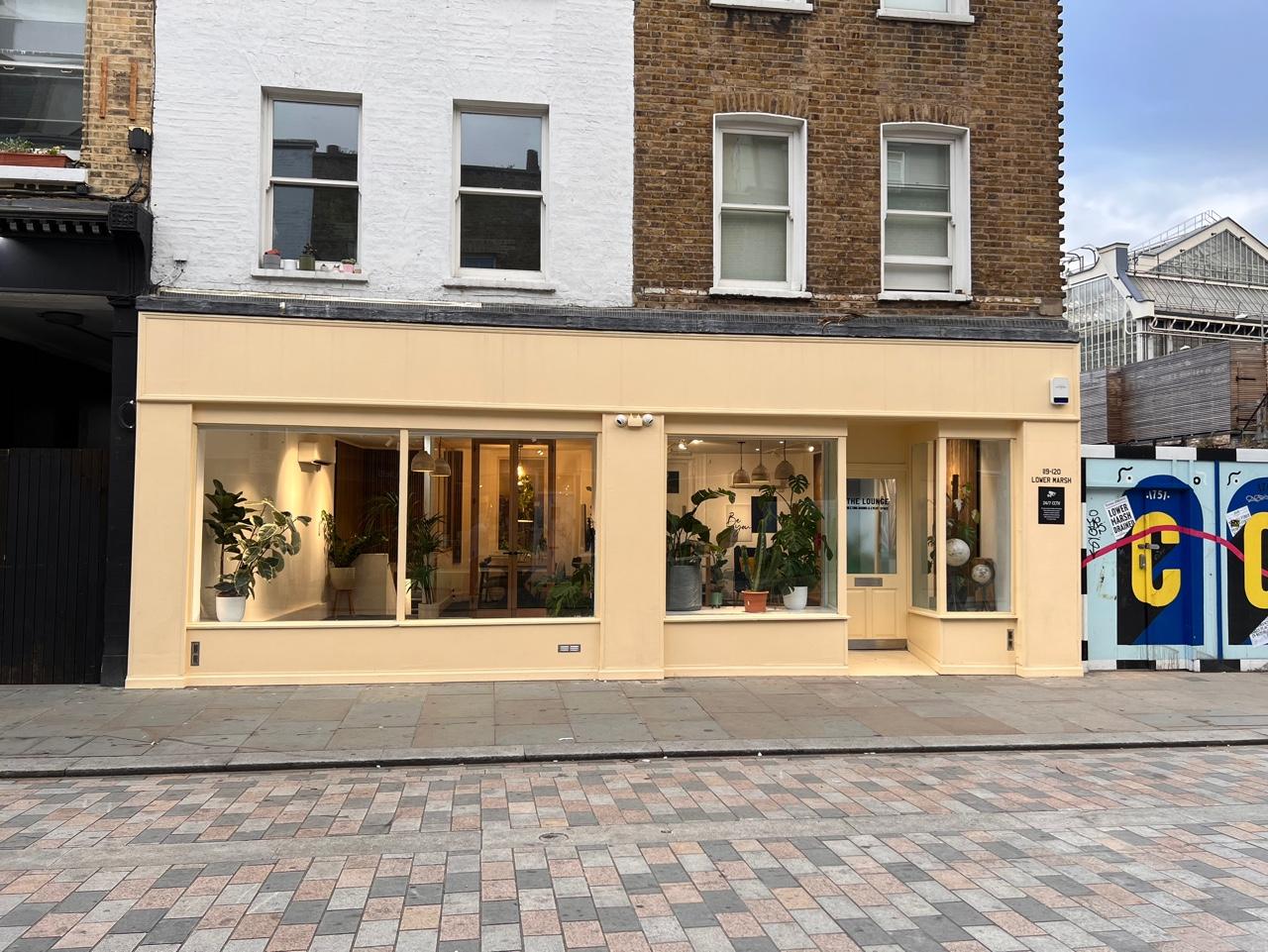 A meeting centre with large front windows, beige exterior, and potted plants at The Travel Cafe Lounge.