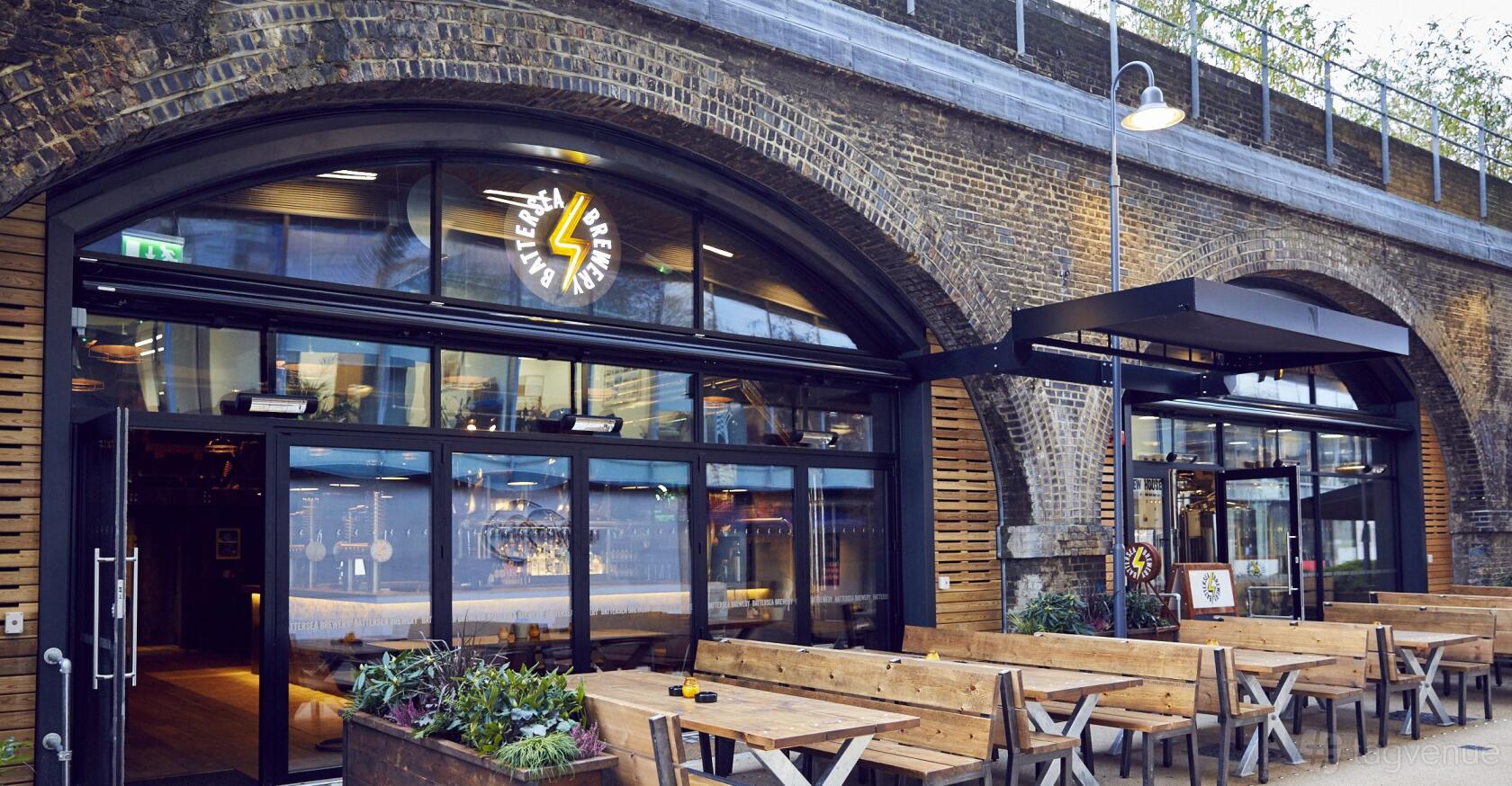 A pub with wooden picnic tables on a covered patio beneath a brick railway arch at Battersea Brewery.