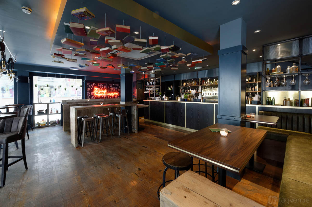 An event space in a cocktail bar with suspended book decor, wood floors, and a backlit bar at Clerkenwell and Social.