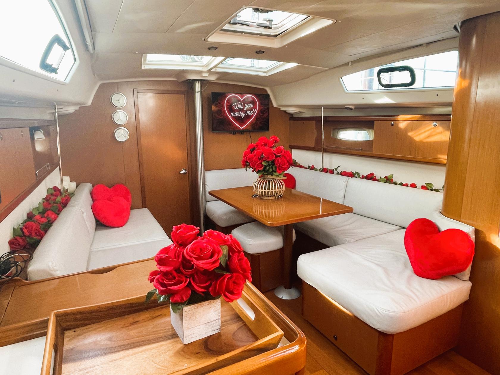 A boat interior with white leather seating, wood accents, red heart pillows, and vases of roses at Go Sailing NYC.