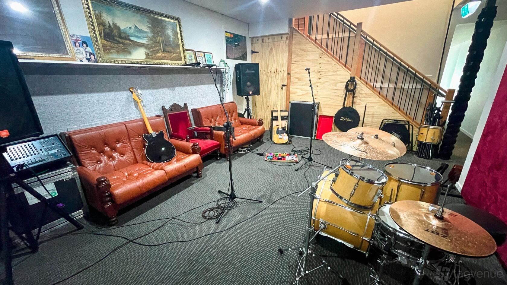 A rehearsal room with vintage sofas, a drum set, guitars, and amplifiers at Elusive Creative.