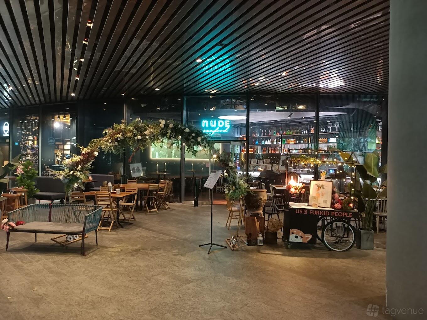 A restaurant terrace with wooden tables, floral archways, and greenery beside the bar at NUDE Grill.