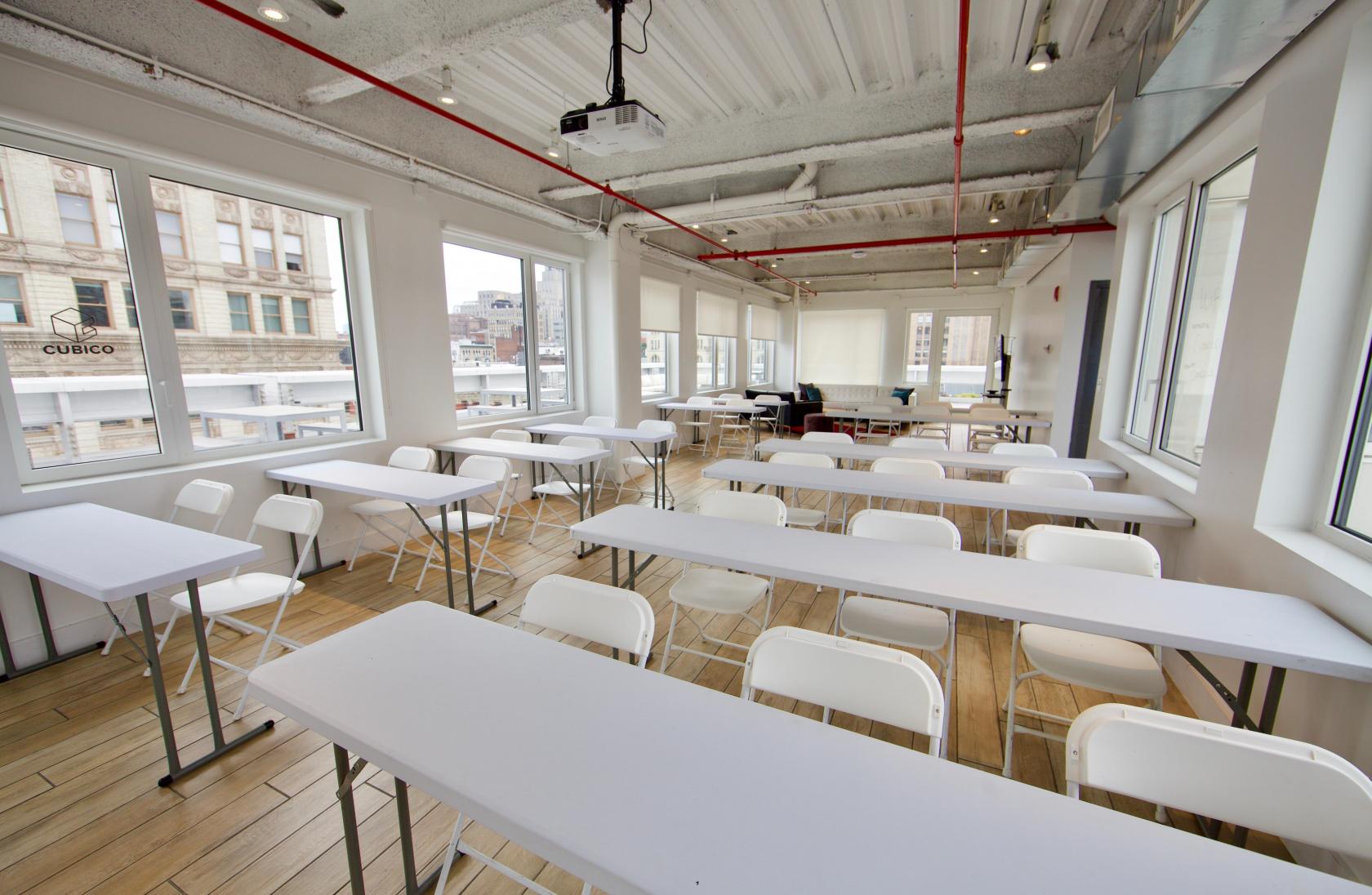 An event space with large windows, white folding chairs, and rectangular tables at Cubico Offices.