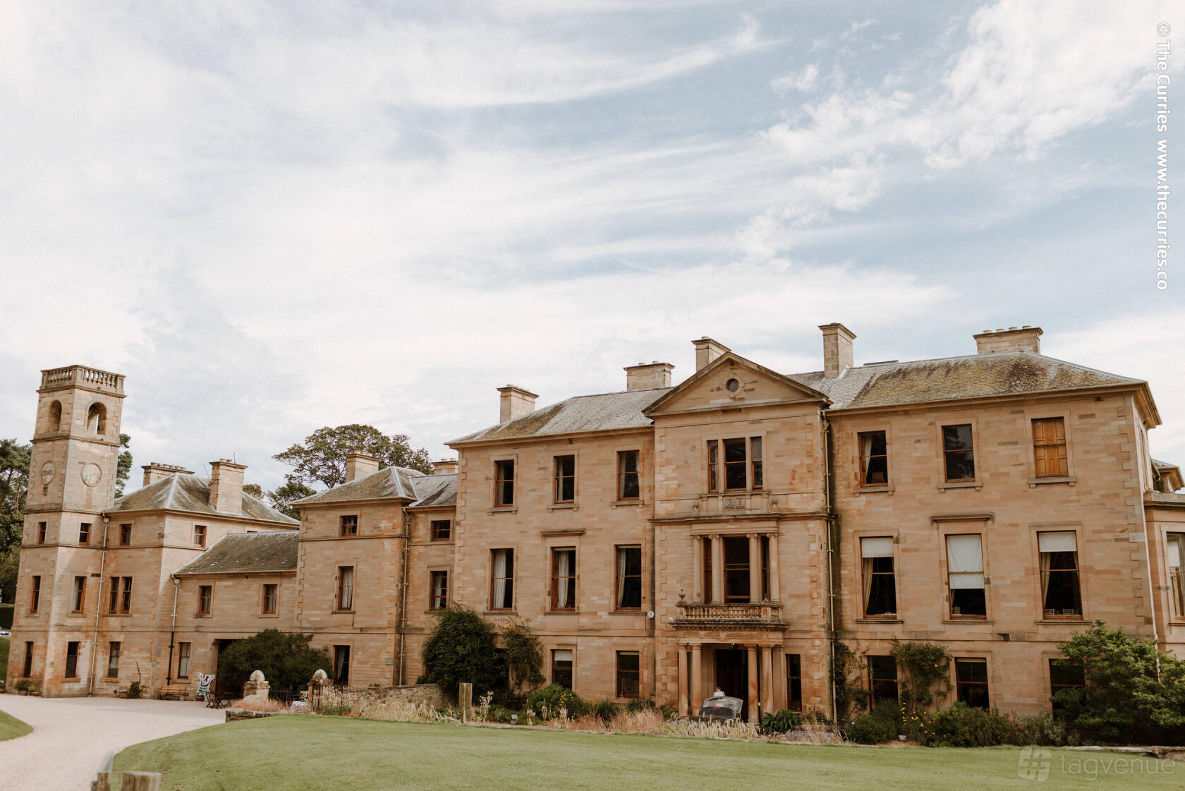 A historic stone building with tall windows and a central entrance surrounded by lawns at Cambo House & Estate.