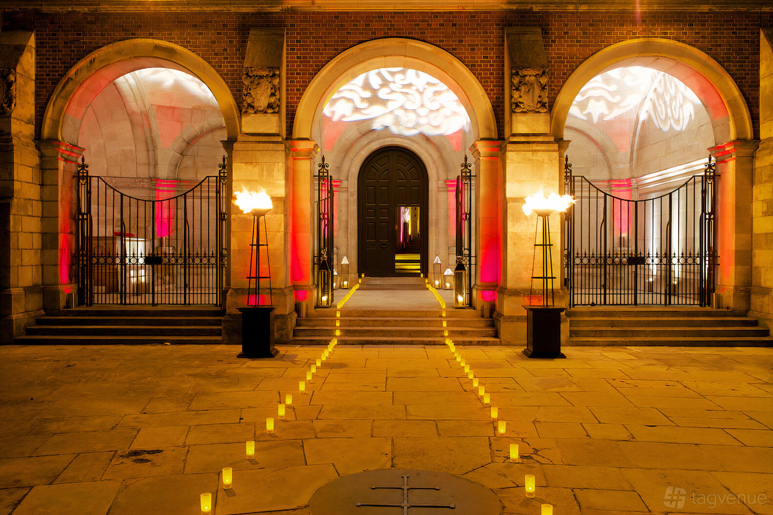 An event space with large stone arches, decorative uplighting, and a pathway of candles at Harrow School War Memorial Vestibule.
