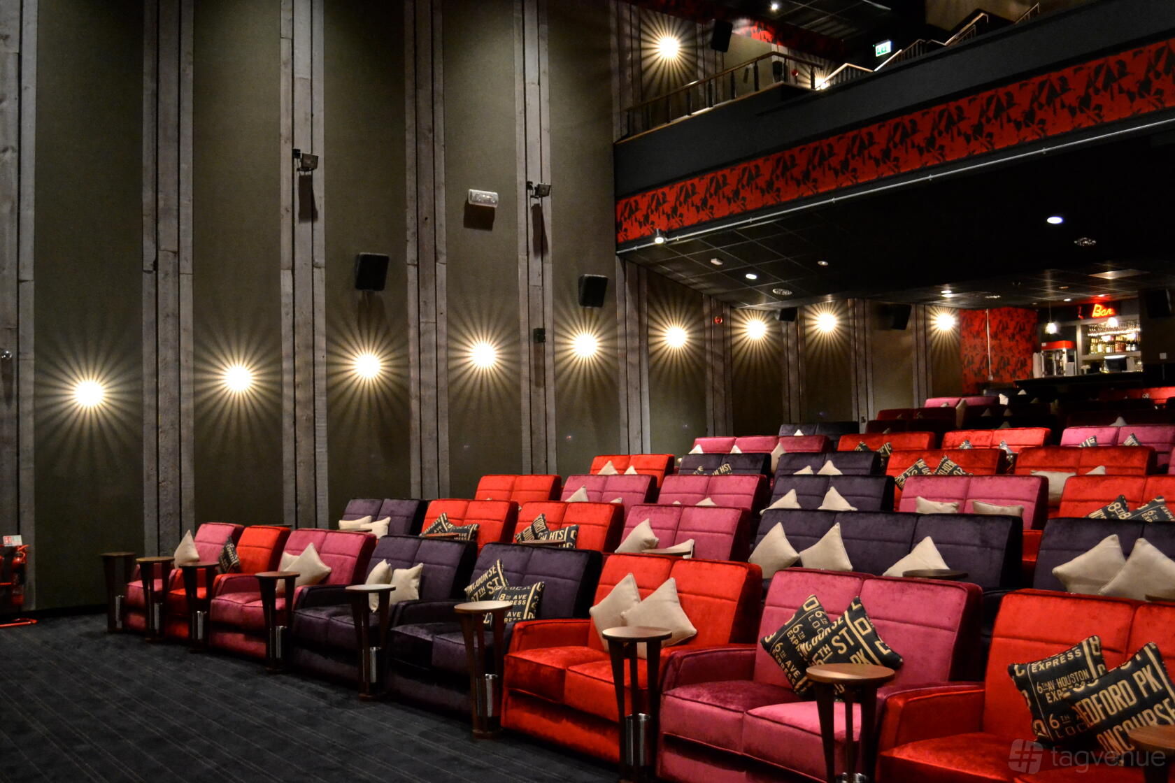 An auditorium with plush red and purple sofas, small tables, and wall-mounted lights at Everyman Leeds.