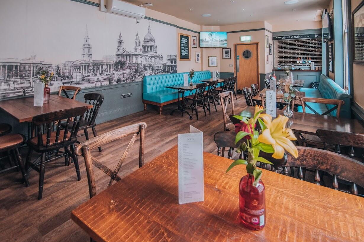 A pub with wooden tables, a blue tufted banquette, and a mural of London landmarks at The Flying Horse.