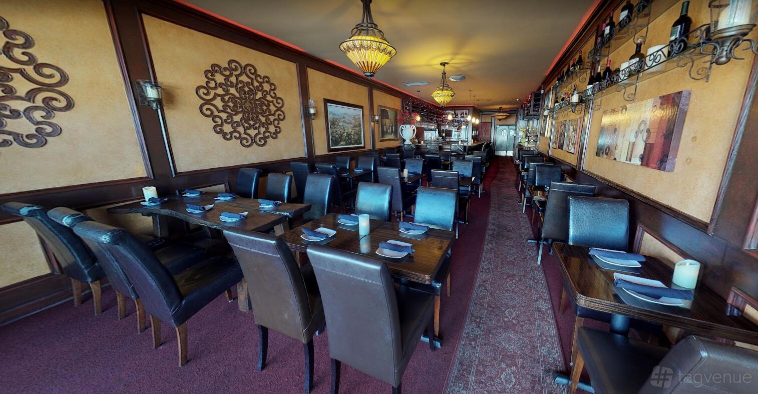 A bar with dark wood tables, leather chairs, wrought-iron wall art, and chandeliers at Vino Wine & Tapas Room.