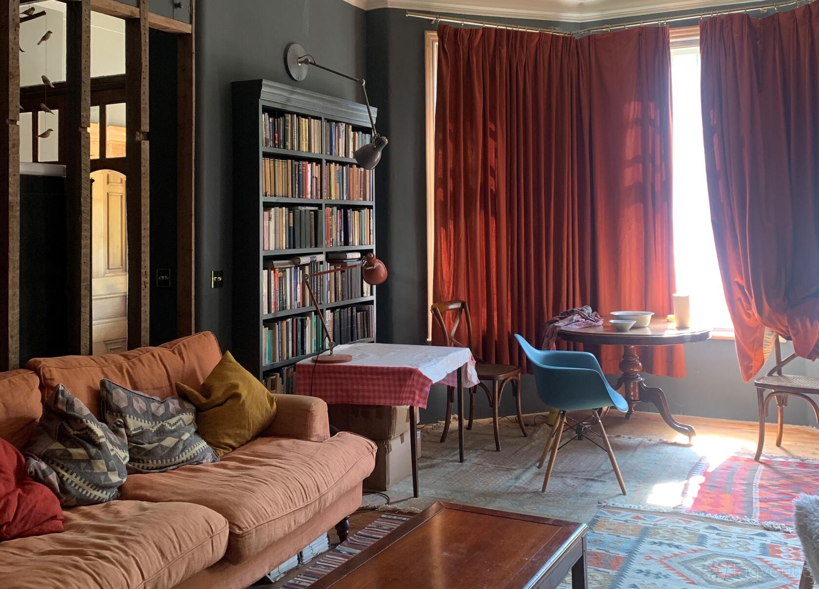 A cozy living room with a peach sofa, patterned pillows, bookshelves, and red curtains at 12 Wellfield Avenue.