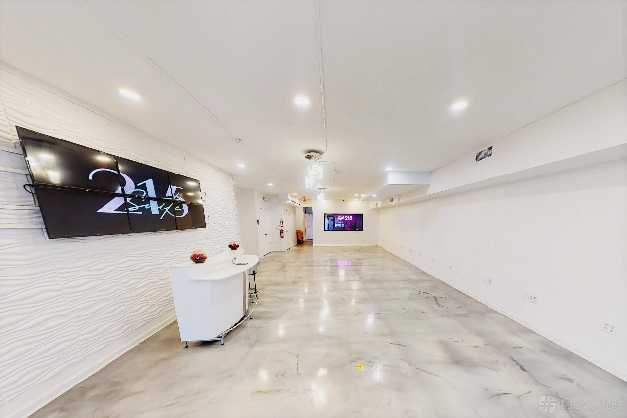 An event venue with polished concrete floors, textured white walls, ceiling lights, and wall-mounted screens at Suite 215.