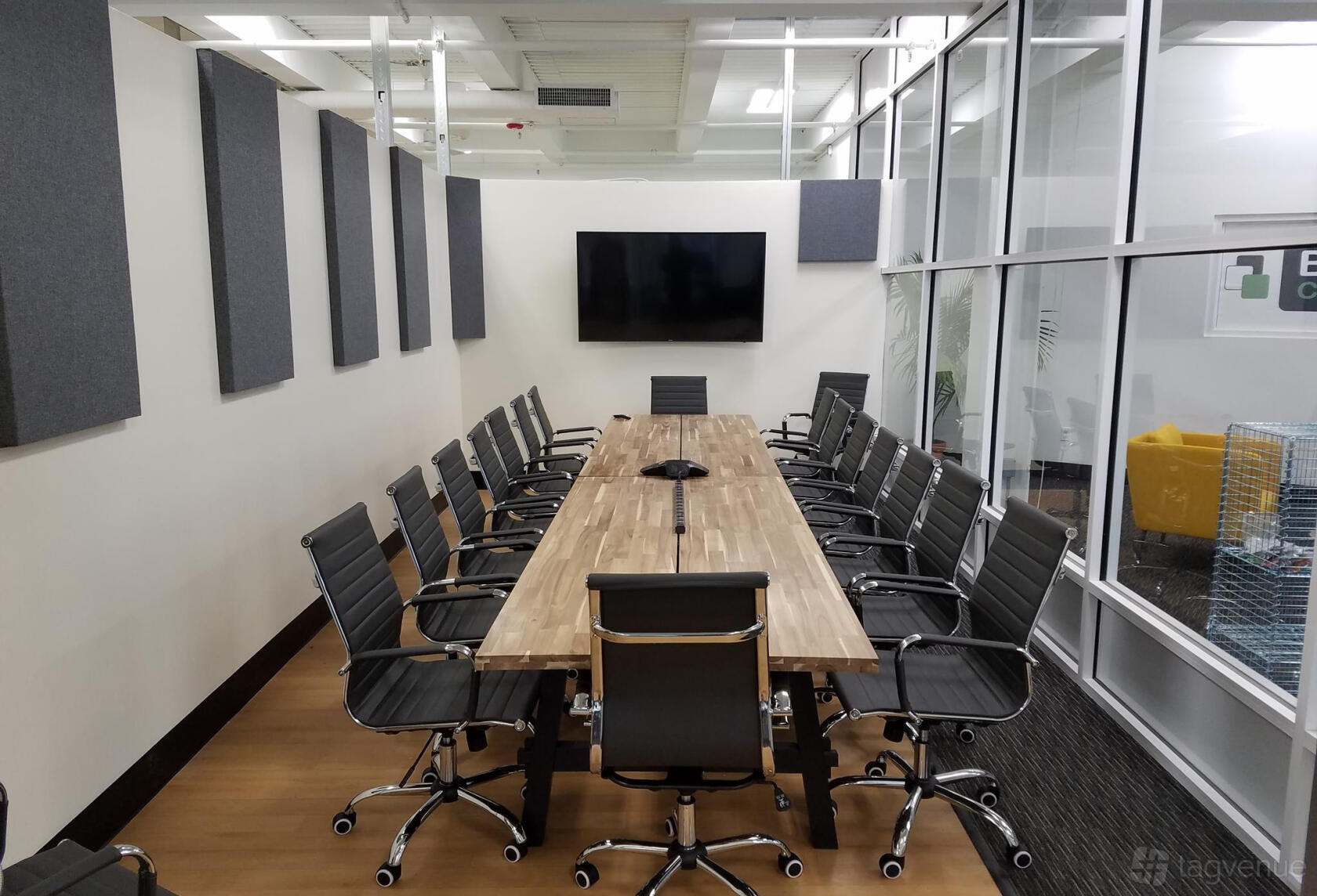 A meeting room with a long wooden conference table, black office chairs, and a wall-mounted screen at Bronx Coworking Space.