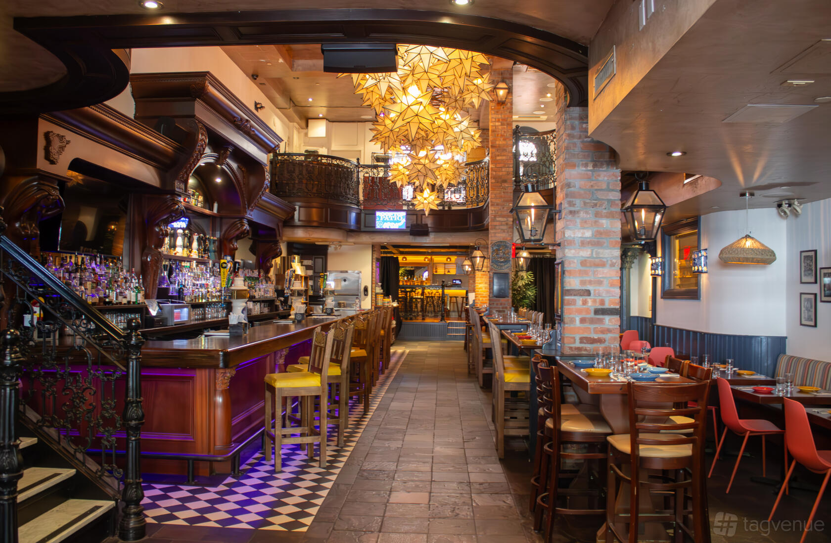 A restaurant with a long wooden bar, colorful chairs, tiled floors, and decorative lighting at Backstage Tavern.