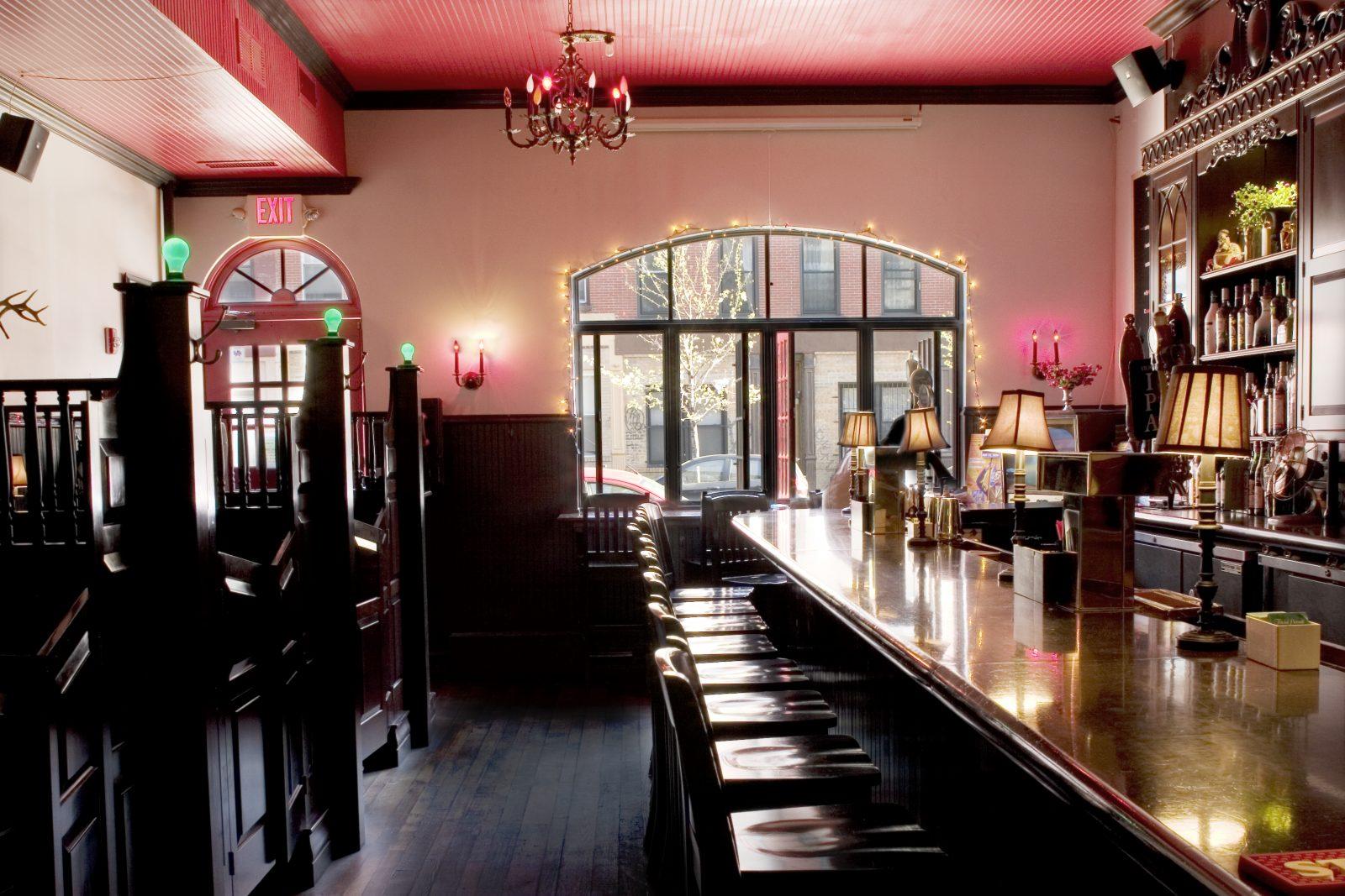 A bar with a long polished wood counter, barstools, vintage lamps, and string lights at Black Rabbit.